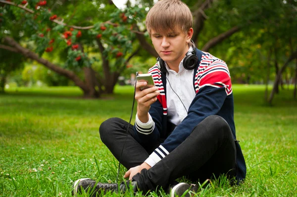 Студент на улице сидит на зеленой траве и слушает музыку через ч — стоковое фото
