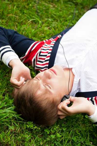 Estudante do lado de fora deitado na grama e ouvir música escola. Fócio — Fotografia de Stock