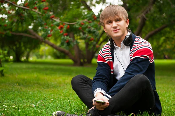 Student sitzt draußen auf grünem Gras und hört Musik über h — Stockfoto