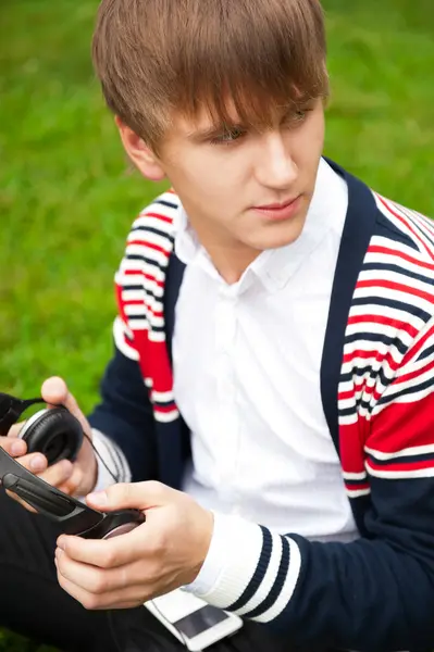 Student outside sitting on green grass and listening music via h — Stock Photo, Image