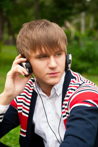 Student outside sitting on green grass and listening music via h — Stock Photo, Image