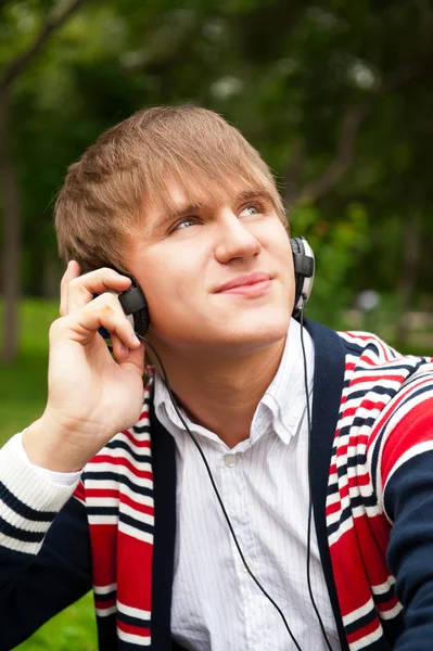 Student utanför sitter på grönt gräs och lyssnar musik via h — Stockfoto