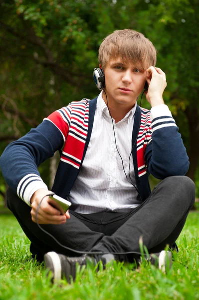 Étudiant assis dehors sur l'herbe verte et écouter de la musique via h — Photo