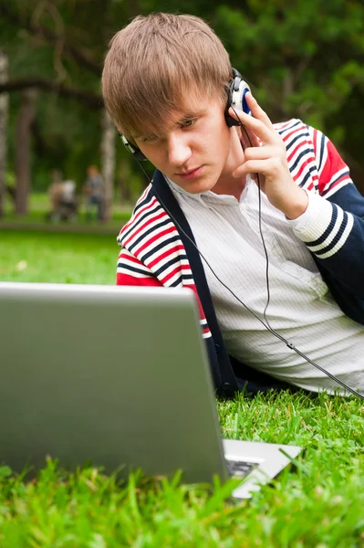 Estudiante acostado en la hierba y el uso de ordenador portátil fuera de la escuela —  Fotos de Stock