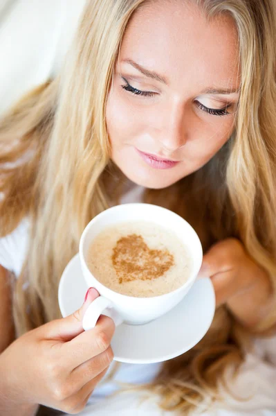 Mosolygó nő iszik egy kávét, feküdt egy ágyban otthon vagy a hotel. — Stock Fotó