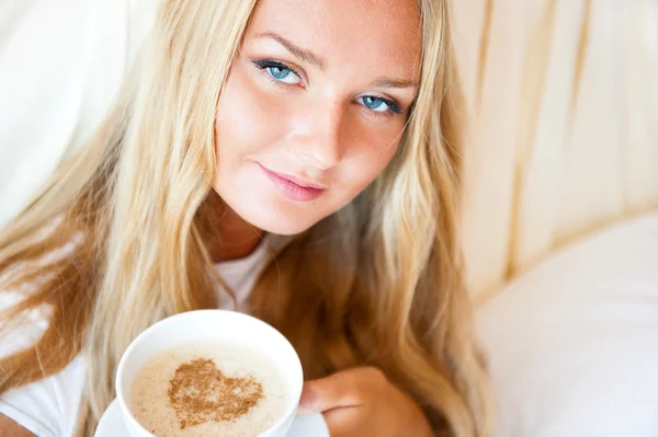 ホテル、自宅のベッドに横になっているコーヒーを飲む女性の笑みを浮かべてください。. — ストック写真