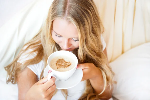 ホテル、自宅のベッドに横になっているコーヒーを飲む女性の笑みを浮かべてください。. — ストック写真