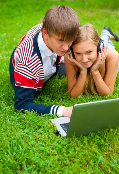 Счастливая молодая пара, используя ноутбук, лежа на траве — стоковое фото