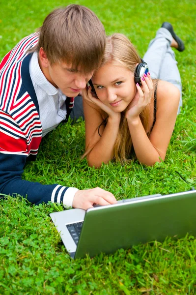 Feliz joven pareja usando el ordenador portátil mientras está acostado en la hierba —  Fotos de Stock
