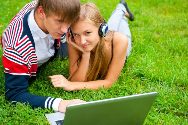 躺在草地上同时使用便携式计算机的快乐年轻夫妇 — 图库照片