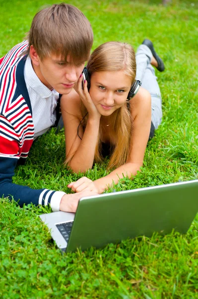 躺在草地上同时使用便携式计算机的快乐年轻夫妇 — 图库照片