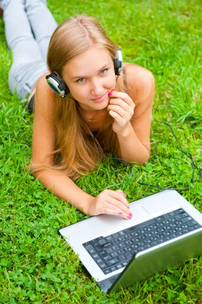 Une jeune fille souriante avec ordinateur portable en plein air écouter de la musique par hea — Photo