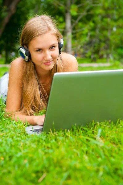 Усміхнена молода дівчина з ноутбуком на відкритому повітрі слухає музику — стокове фото