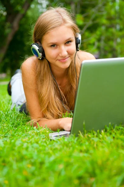 Улыбающаяся молодая девушка с ноутбуком на улице слушает музыку хеа — стоковое фото