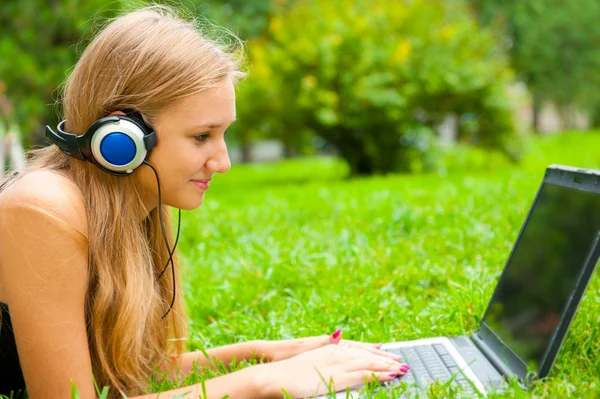 Ένα χαμογελαστό νεαρό κορίτσι με το lap-top υπαίθρια ακούγοντας μουσική από hea — Φωτογραφία Αρχείου