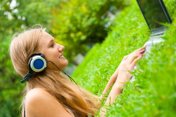 Una joven sonriente con portátil al aire libre escuchando música por hea —  Fotos de Stock