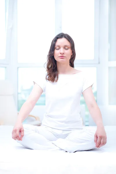 Mujer joven meditando con los ojos cerrados en el dormitorio luminoso sittin — Foto de Stock