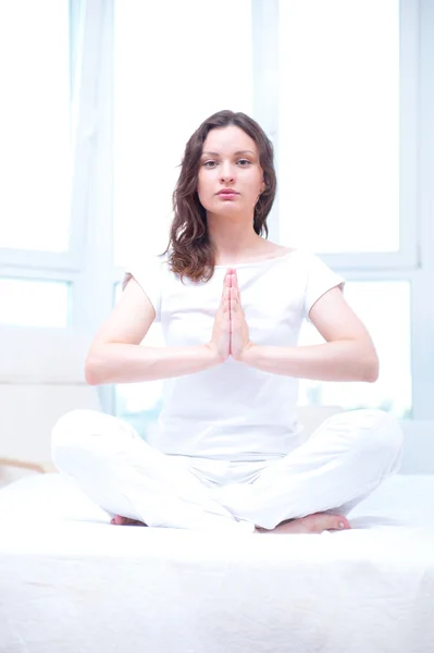 Молодая женщина медитирует с закрытыми глазами в яркой спальне сидя — стоковое фото