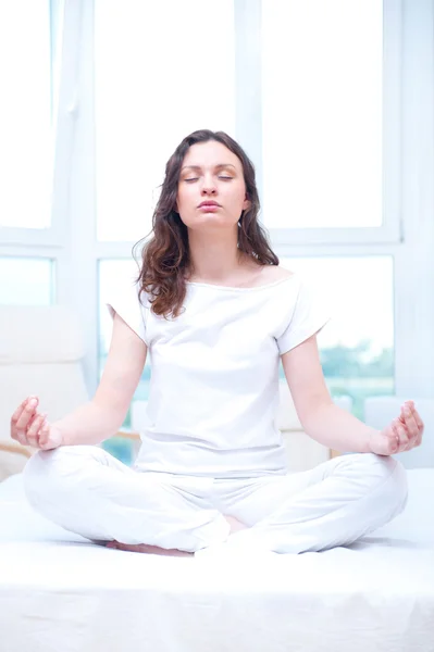 Jonge vrouw met gesloten ogen in heldere slaapkamer sittin mediteren — Stockfoto