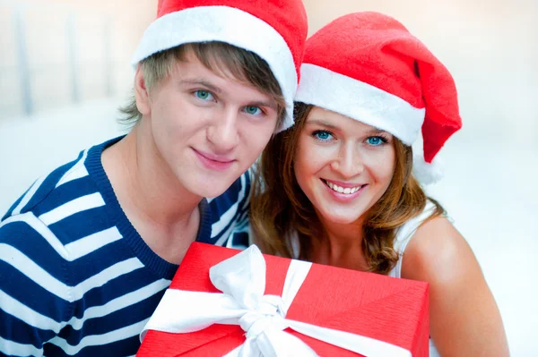 Porträt eines jungen hübschen Paares, das drinnen steht und Weihnachtsmann trägt — Stockfoto