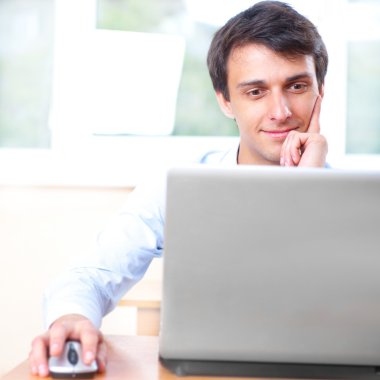 ofisinde bir laptop önünde oturan bir genç adam
