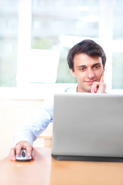 Um jovem sentado na frente de um laptop em seu escritório — Fotografia de Stock