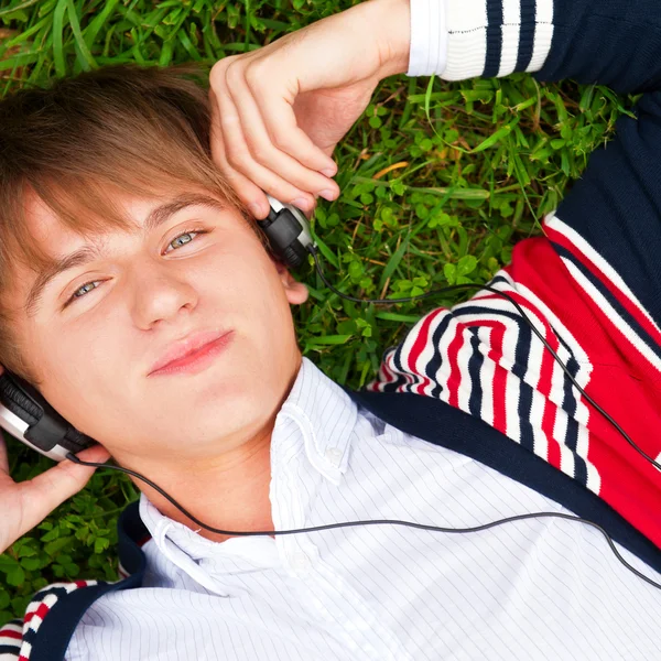 Student outside laying on grass and listening music school. Phot — Stock Photo, Image