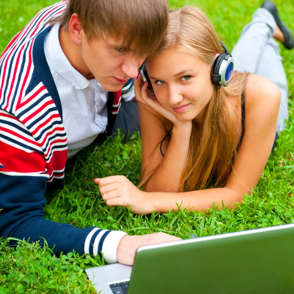Šťastný mladý pár pomocí přenosného počítače a zároveň leží na trávě — Stock fotografie