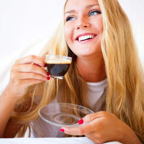 Donna sorridente che beve un caffè sdraiata su un divano a casa — Foto Stock