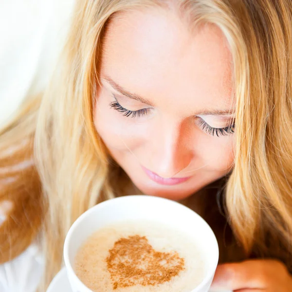 Lächelnde Frau trinkt einen Kaffee, der zu Hause oder im Hotel auf dem Bett liegt. — Stockfoto