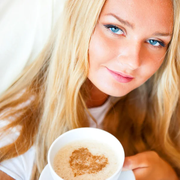 Usmívající se žena pít kávu, ležící na posteli doma nebo v hotelu. — Stock fotografie