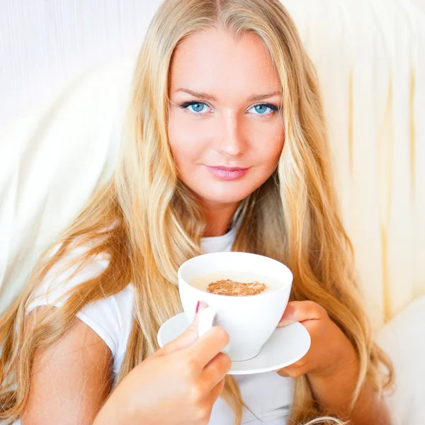 Lächelnde Frau trinkt einen Kaffee, der zu Hause oder im Hotel auf dem Bett liegt. — Stockfoto