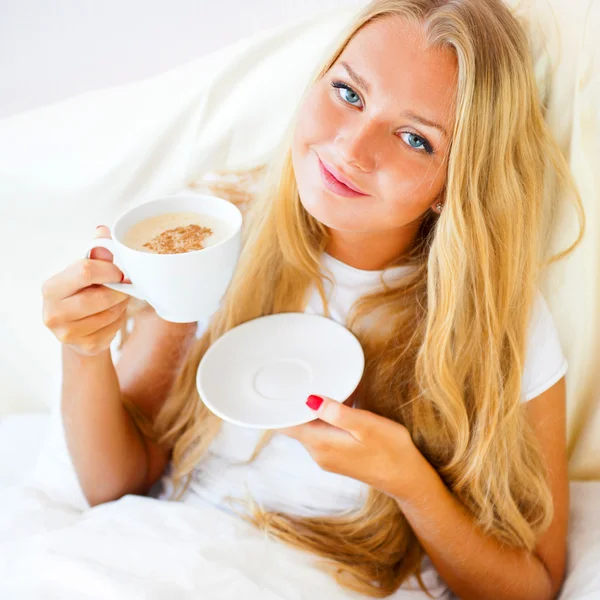 Jonge vrouw thuis nippen thee of koffie uit een beker — Stockfoto