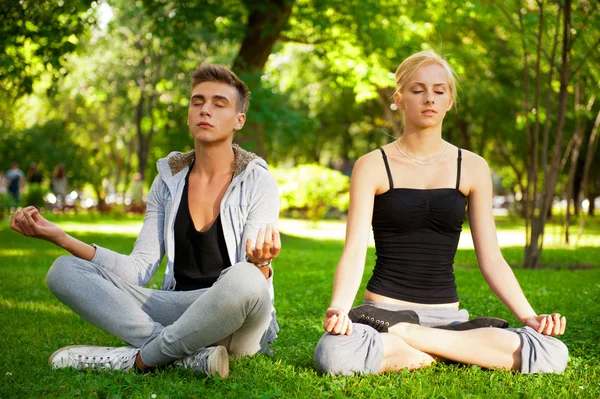 Portrait of young beautiful couple sitting in lotus pose on gree — Stock Photo, Image