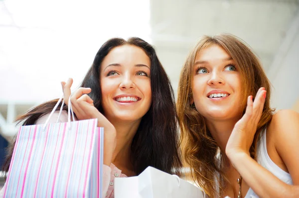 Duas mulheres de compras animadas juntas dentro do shopping. Horizontes Imagens Royalty-Free