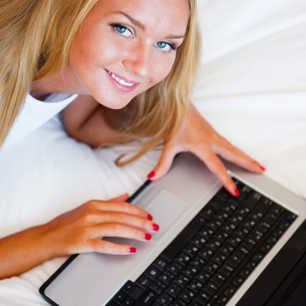 Χαμογελαστή γυναίκα χρησιμοποιώντας ένα φορητό υπολογιστή ενώ βρίσκεται στο κρεβάτι της — Φωτογραφία Αρχείου