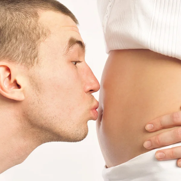 Man kissing his wife's belly at home against wall — Stock Photo, Image