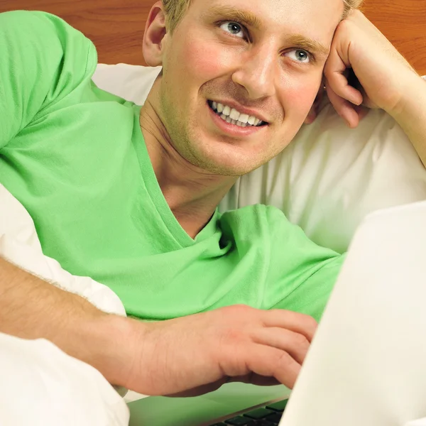 Attractive man relaxing in bed. White silk linen. Working by is — Stock Photo, Image