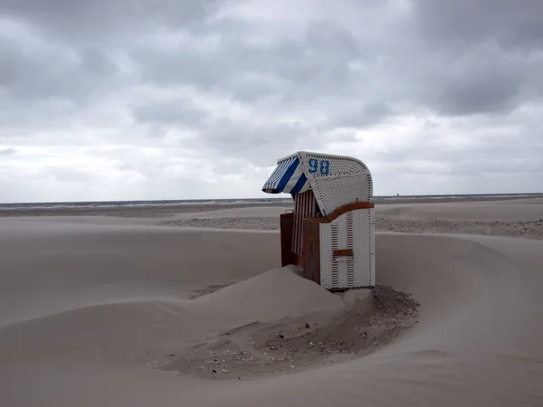 Cadeira de praia depois de uma tempestade com pequenas dunas de areia se formando em torno dela — Fotografia de Stock