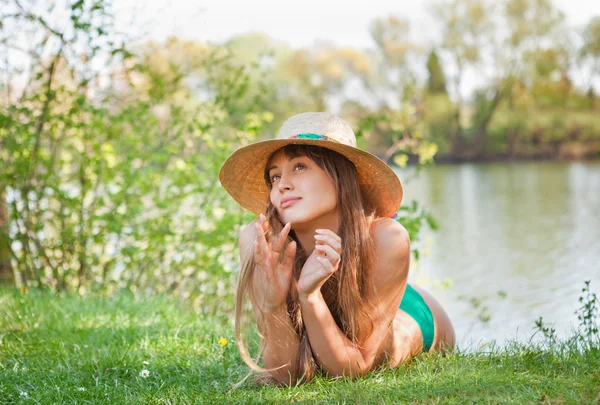 Chica rubia joven con un sombrero acostado en la hierba —  Fotos de Stock