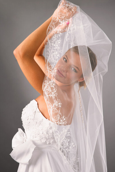 Beautiful bride under veil on studio neutral background