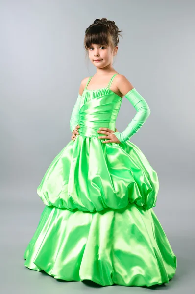 Милая маленькая девочка позирует на студийном нейтральном фоне в великолепном зеленом платье — стоковое фото