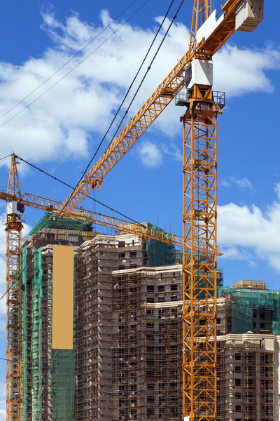 Construction of multi-storey complex with construction cranes on blue sky background.
