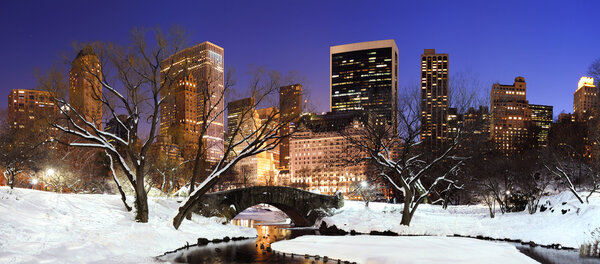 New York City Manhattan Central Park panorama in winter with snow, bridge, freezing lake and skyscrapers at dusk.