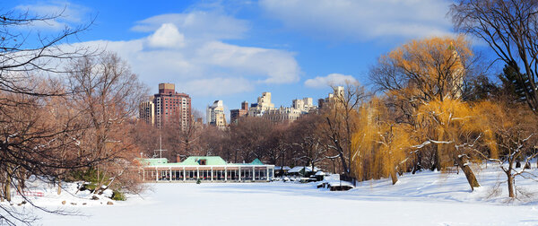 New York City Manhattan Central Park panorama in winter with ice and snow over lake with skyscrapers and blue sunny sky at dusk.