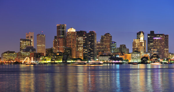 Boston downtown skyline panorama with skyscrapers over water with reflections at dusk illuminated with lights.