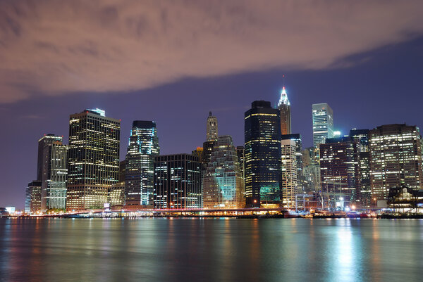 New York City Manhattan skyline with Brooklyn Bridge and office skyscrapers building in at dusk illuminated with lights at night over Hudson River
