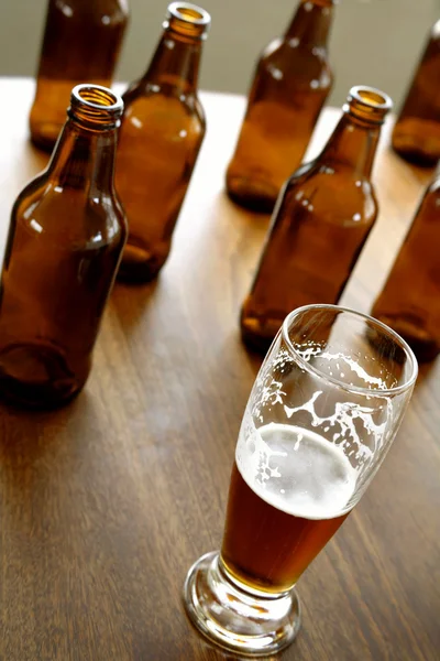 Glass of beer and empty bottles on table — Stock Photo, Image