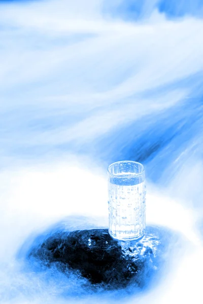 Glass of water on rock in stream — Stock Photo, Image