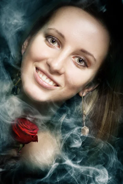 Lächelndes sinnliches Mädchen im Rauch mit einer roten Rose — Stockfoto